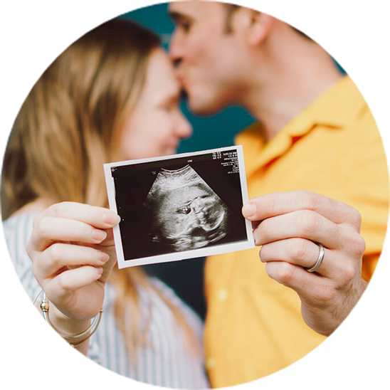 Paar hält Ultraschallbild eines Babys in die Kamera und küsst sich.