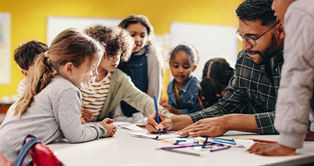 Lehrer und Kinder zeichnen gemeinsam an einem Tisch.