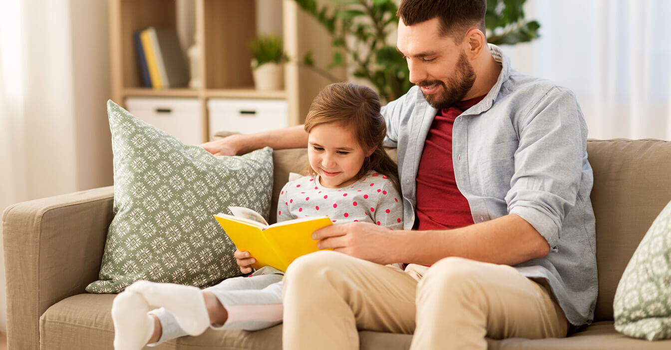 Ein Mann und ein Kind sitzen auf einem Sofa und schauen ein Buch.