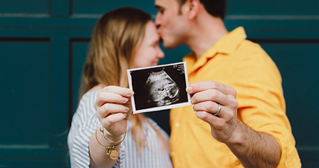  Ein glückliches Paar küsst sich und präsentiert ein Ultraschallbild ihres Babys.